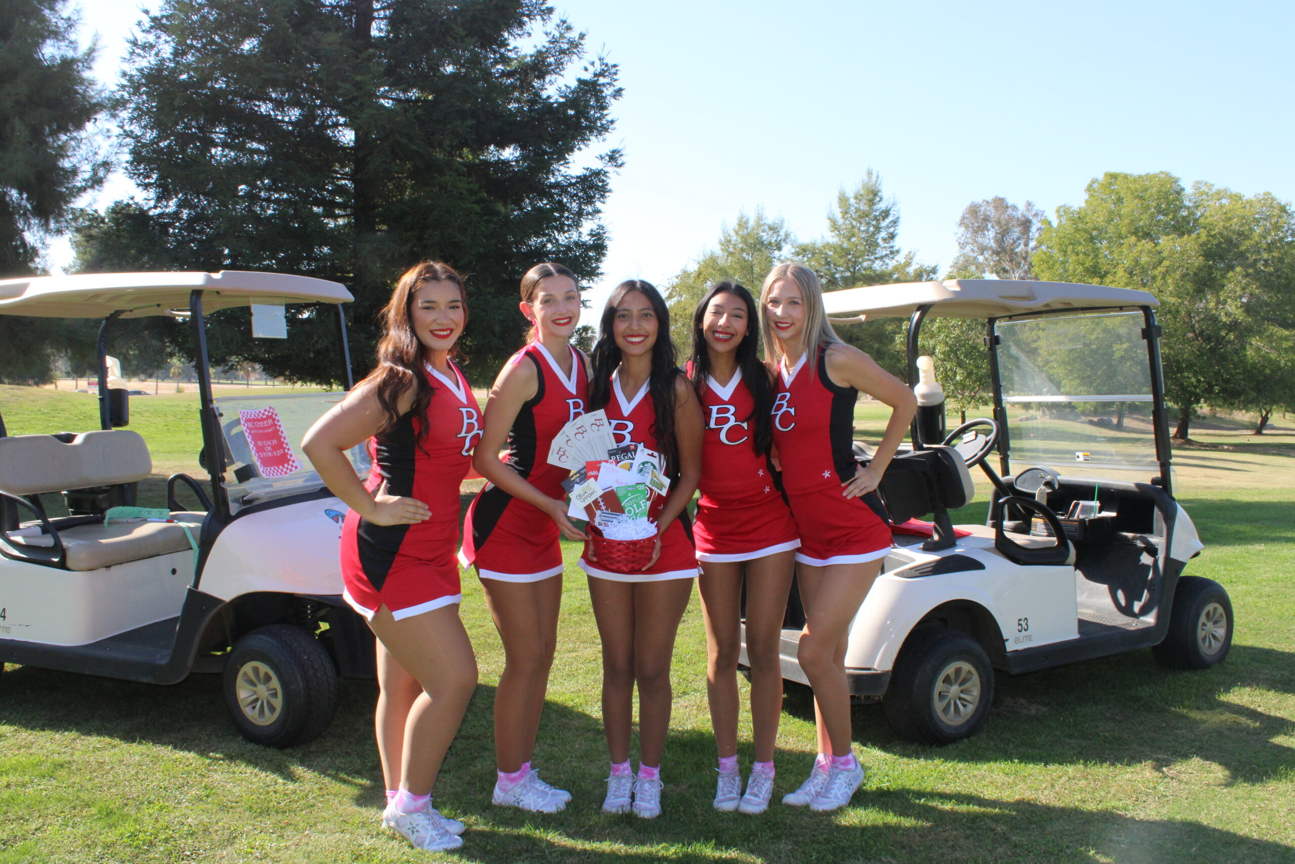 Cheerleaders in front of golf carts holding a raffle basket