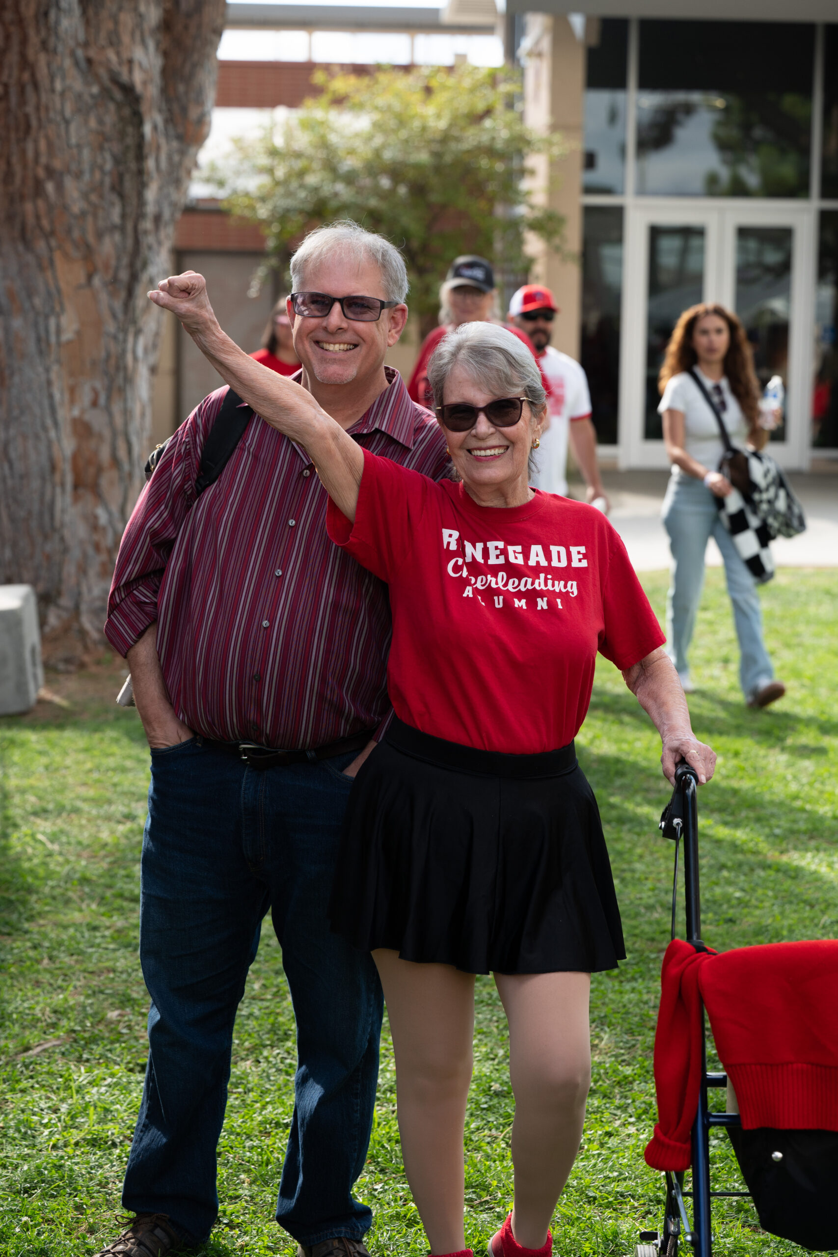 Two smiling Bakersfield College alumni pose together outdoors as one raises her fist in celebration.