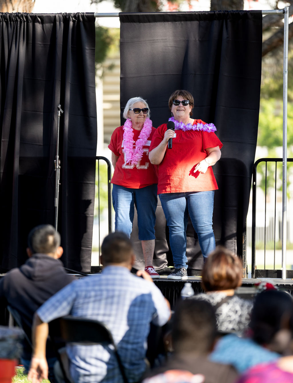 Two women in red shirts and leis speak onstage at the BC Scholarship Celebration.