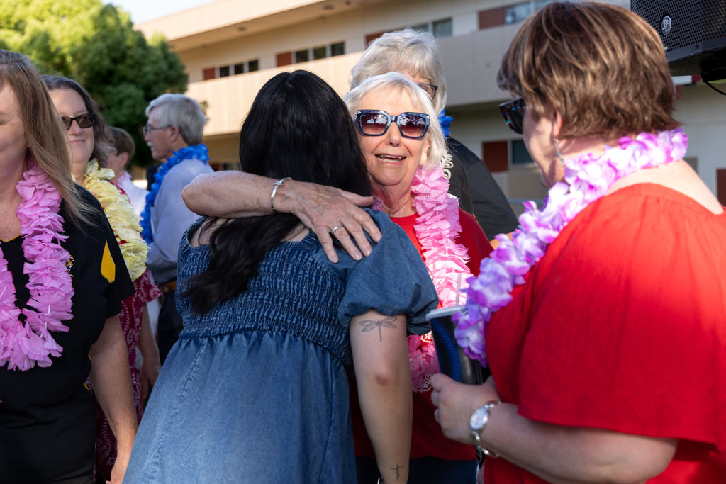 A woman in sunglasses and a pink lei hugs an attendee at the BC Scholarship Celebration.