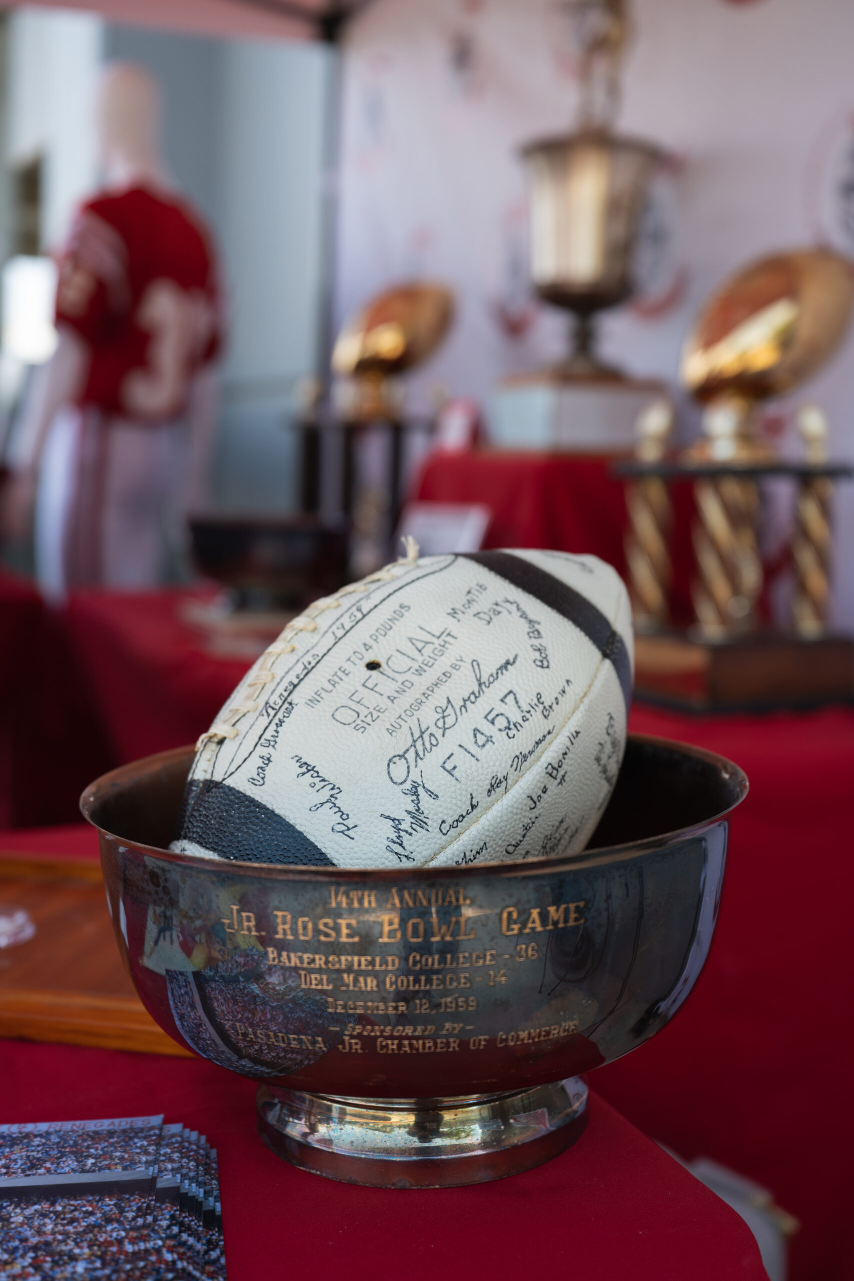 Signed vintage football rests inside the 1959 Junior Rose Bowl trophy.